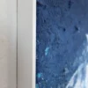 Detailaufnahme des weißen Holzrahmens am Gemälde "Thalassa", seitlicher Blick auf Rahmenkante und strukturierte, blaue Bildoberfläche